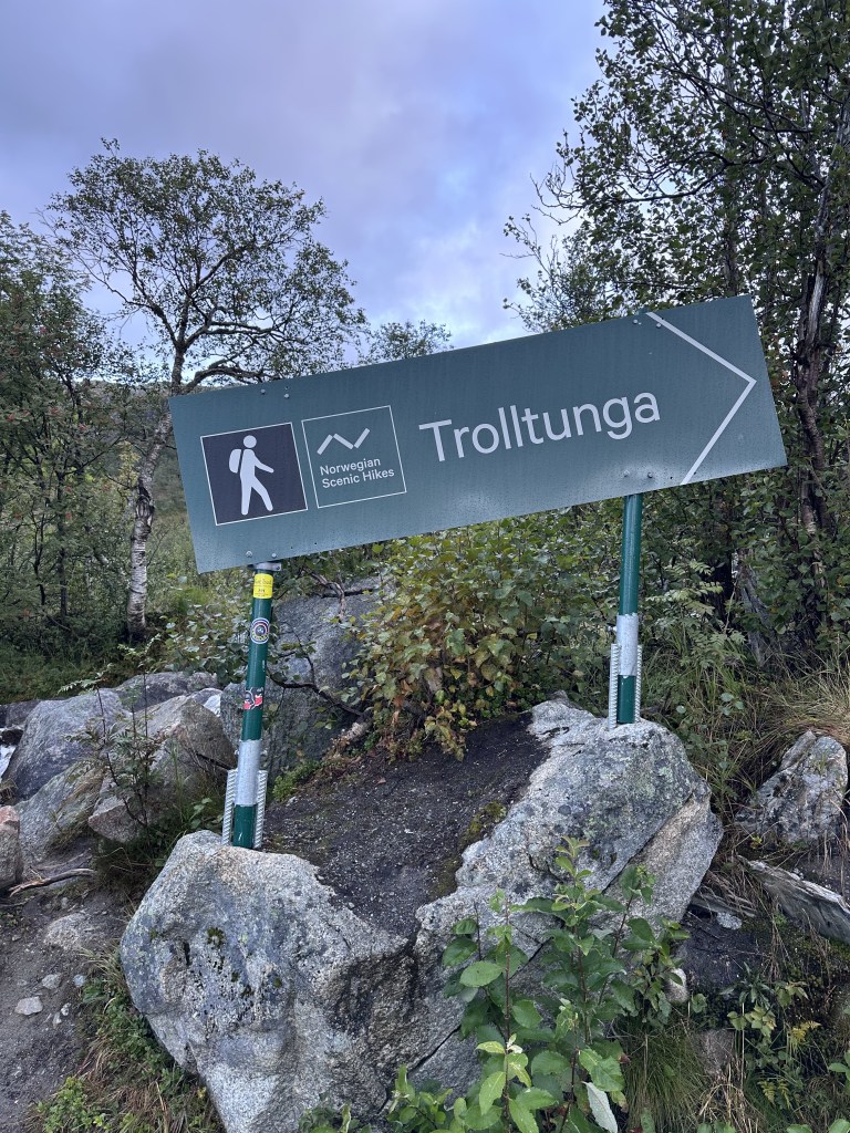Sign pointing to Trolltunga, with symbols for hiking, surrounded by nature.